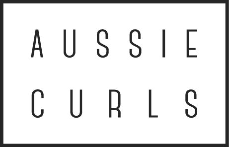 A rectangle white box with black outline inside the rectangle box is the wording Aussie Curls in bold black capital letters 