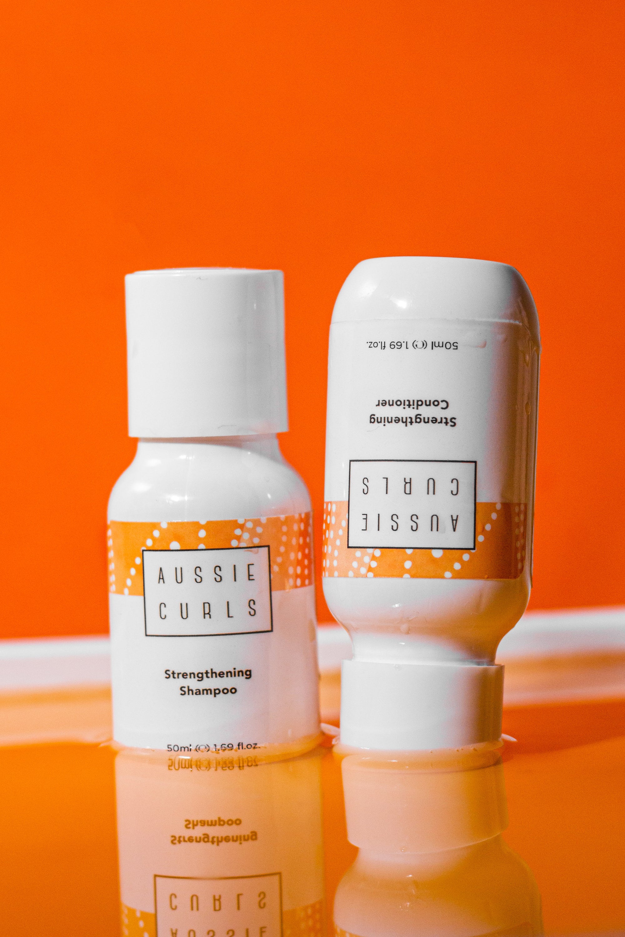 Aussie curls 50ml sample white glossy shampoo bottle with a 50ml sample size white glossy conditoner bottle next to it, the bottles have orange and white indigenous Australian artwork and are on a dark orange and yellow background