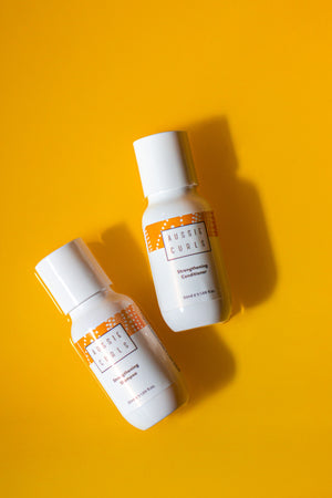 Aussie curls 50ml sample white glossy shampoo bottle with a 50ml sample size white glossy conditoner bottle next to it, the bottles have orange and white indigenous Australian artwork and are on a vibrant yellow background