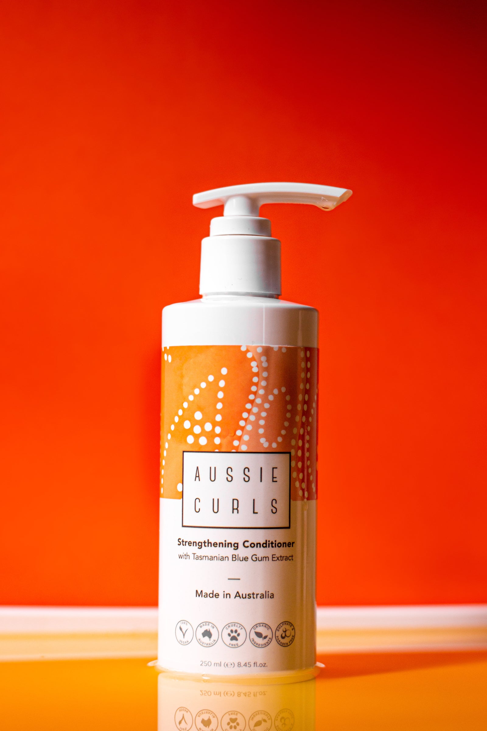 Aussie curls 250ml white glossy conditoner bottle with orange and white indigenous Australian artwork on a dark orange and yellow background 